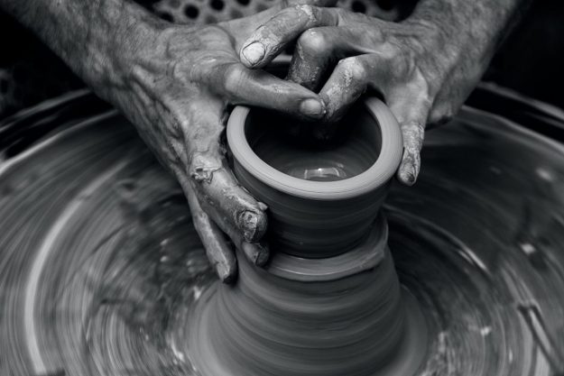 Messy hands sculpting on a pottery wheel in motion