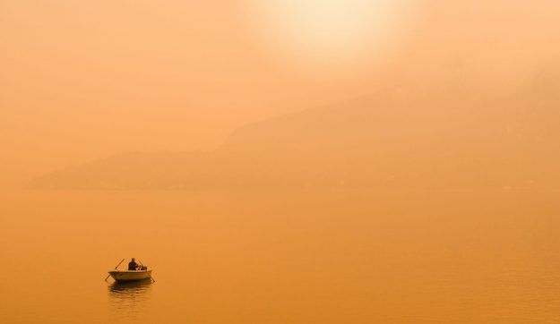 silhouette photography of person in gray sailing boat in the middle of body of water